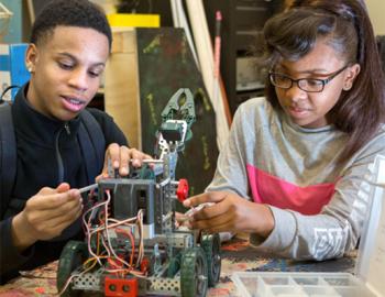 Two high school-aged students working together on building a robot