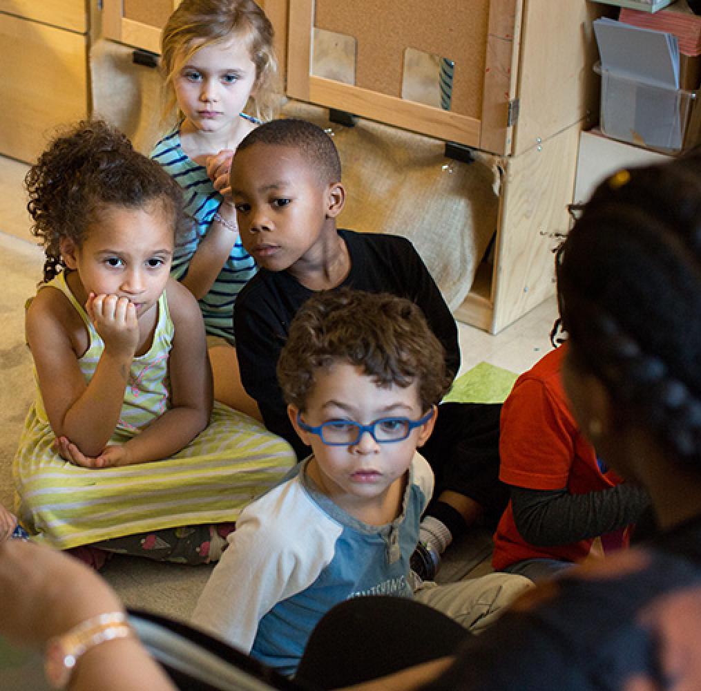 Elementary aged students listening to a teacher read a book