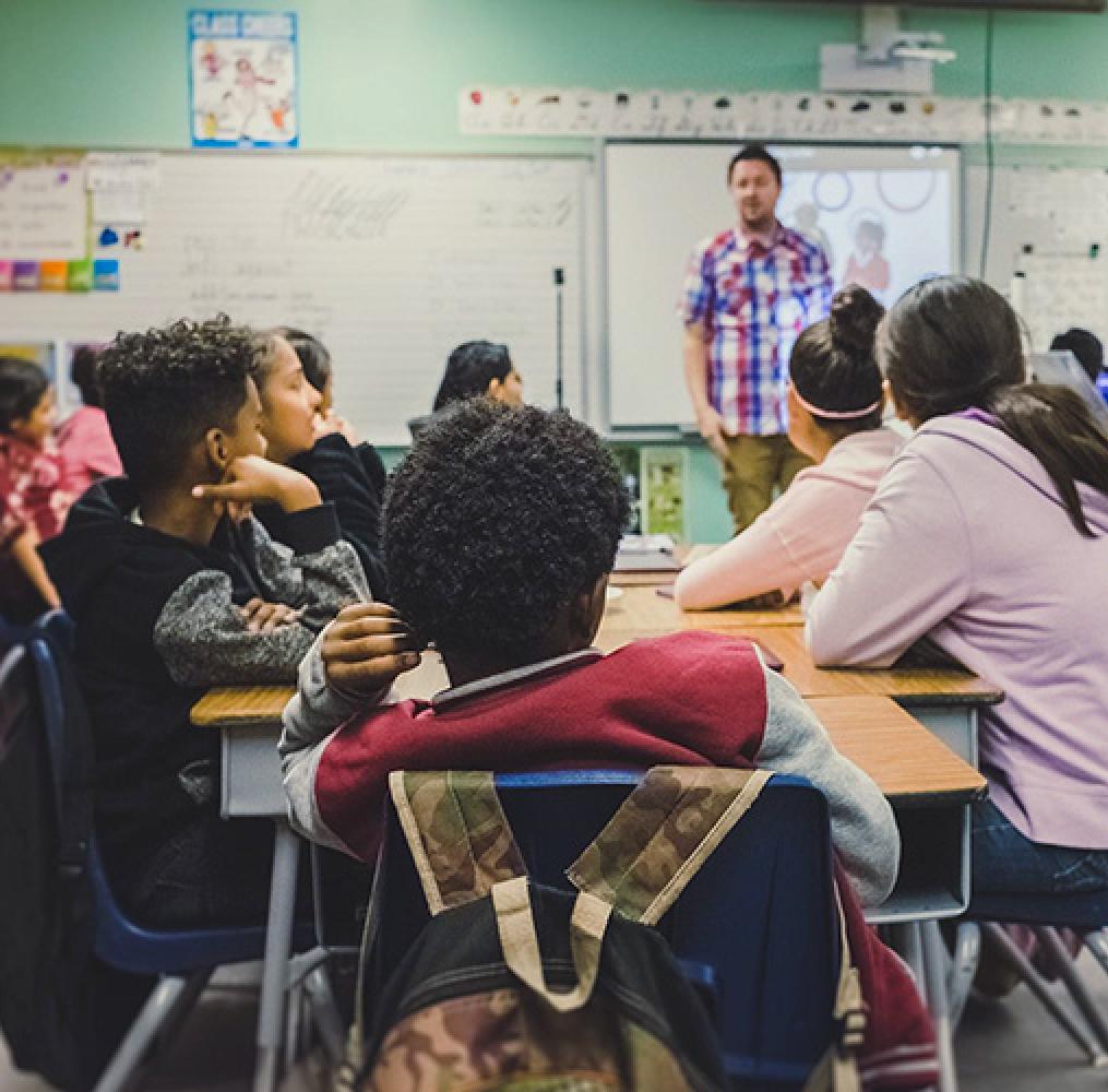 teacher in front of a whiteboard facing high school aged students