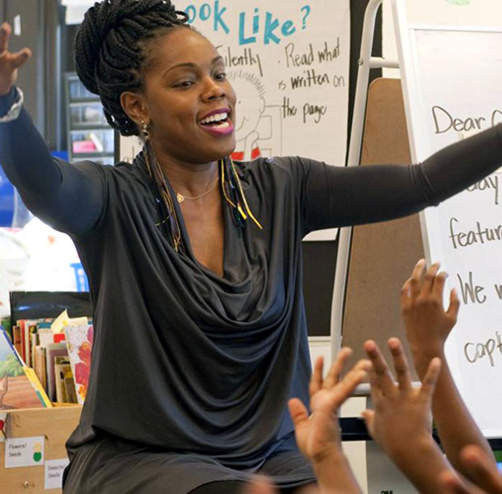 An elementary school teacher with arms raised in front of children