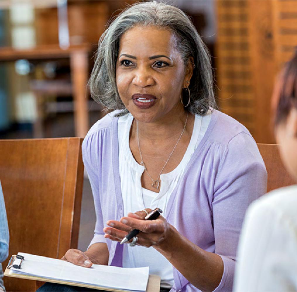 Woman seated holding a clipboard speaking with two adults