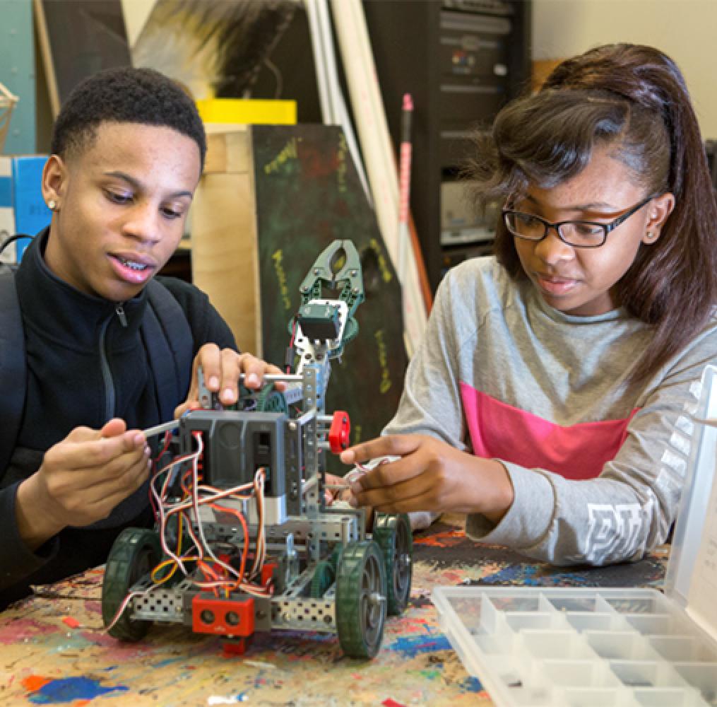 Two high school-aged students working together on building a robot
