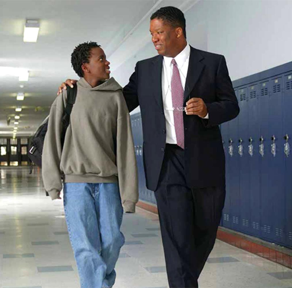 Male educator and male high school-aged student walking in a school hallway