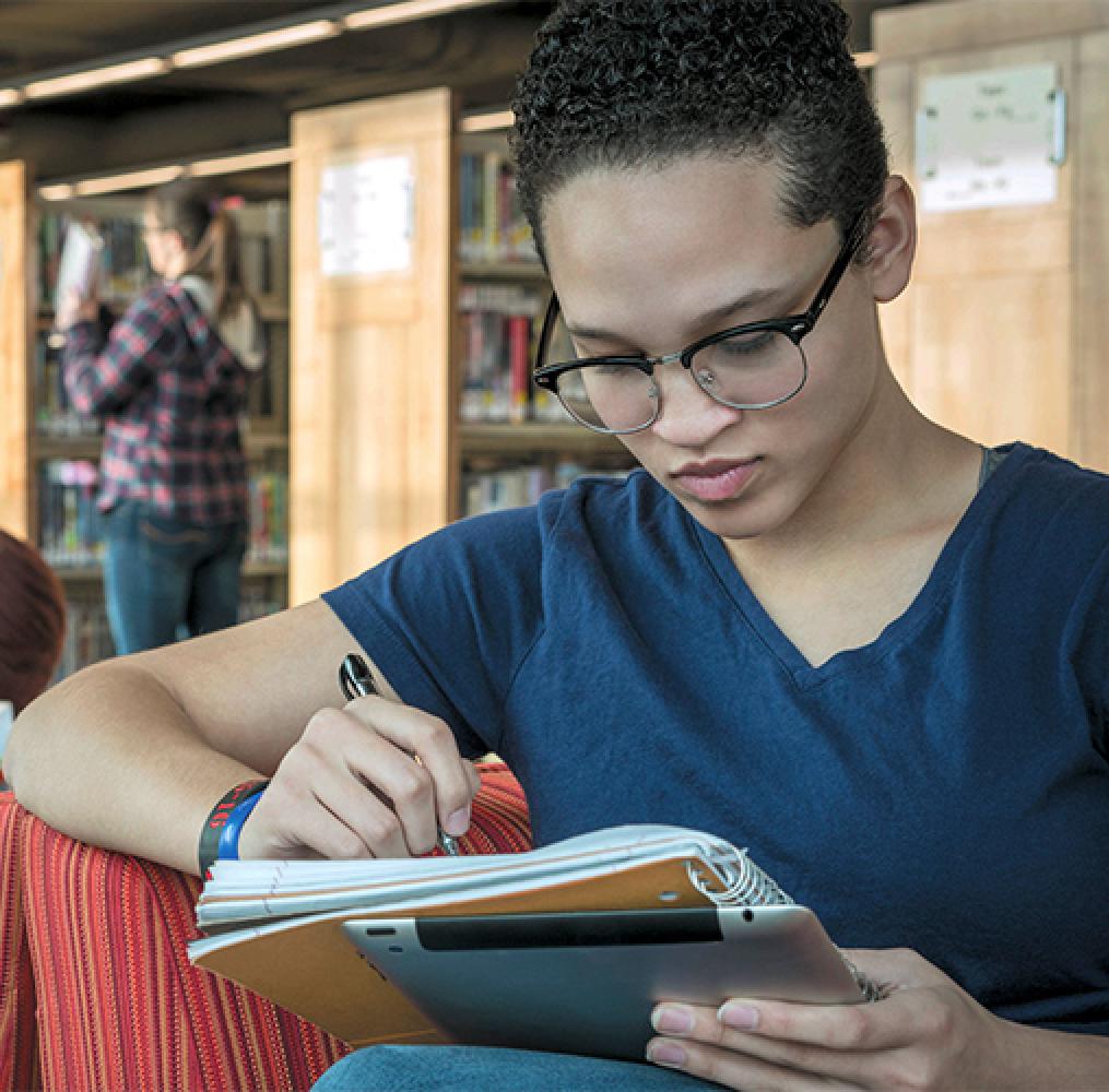 College aged woman writing in a notebook in a library