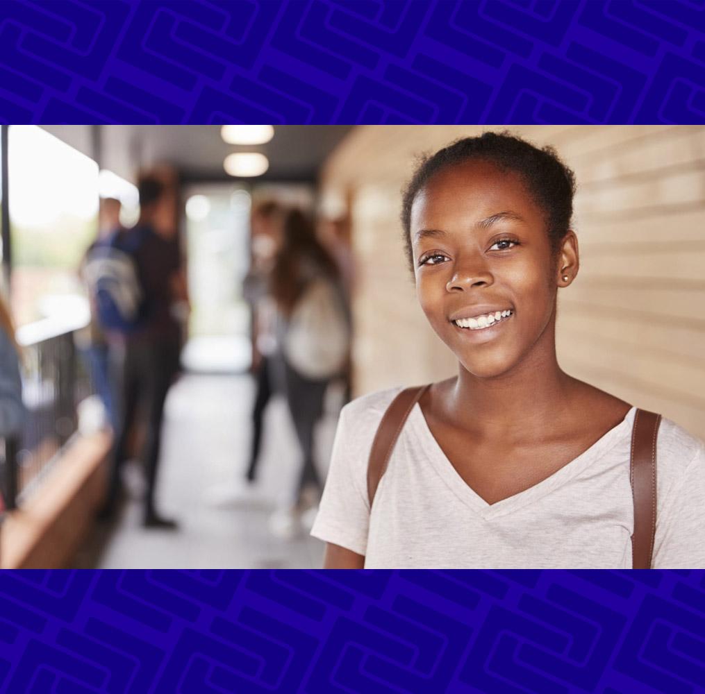 African American girl smiling with a backpack and classmates in the background.