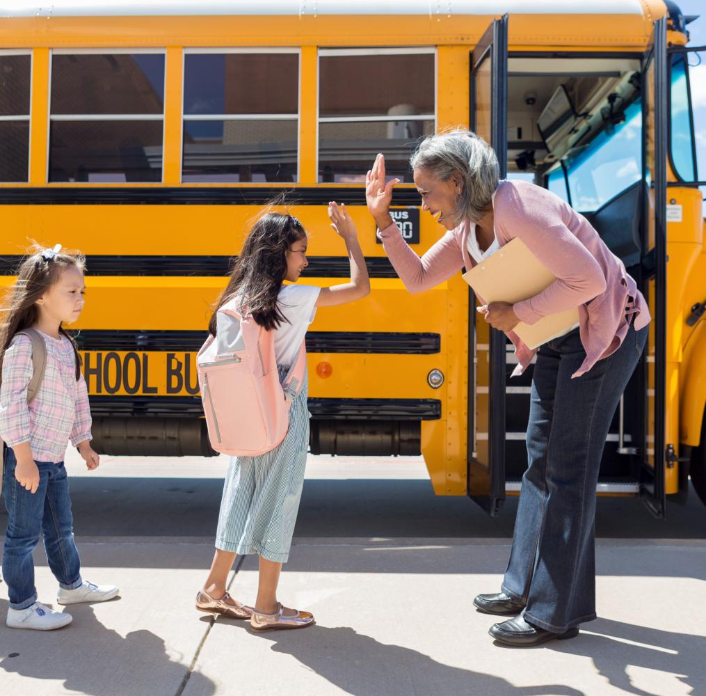 Principal giving an elementary student a high five in from of a school bus.