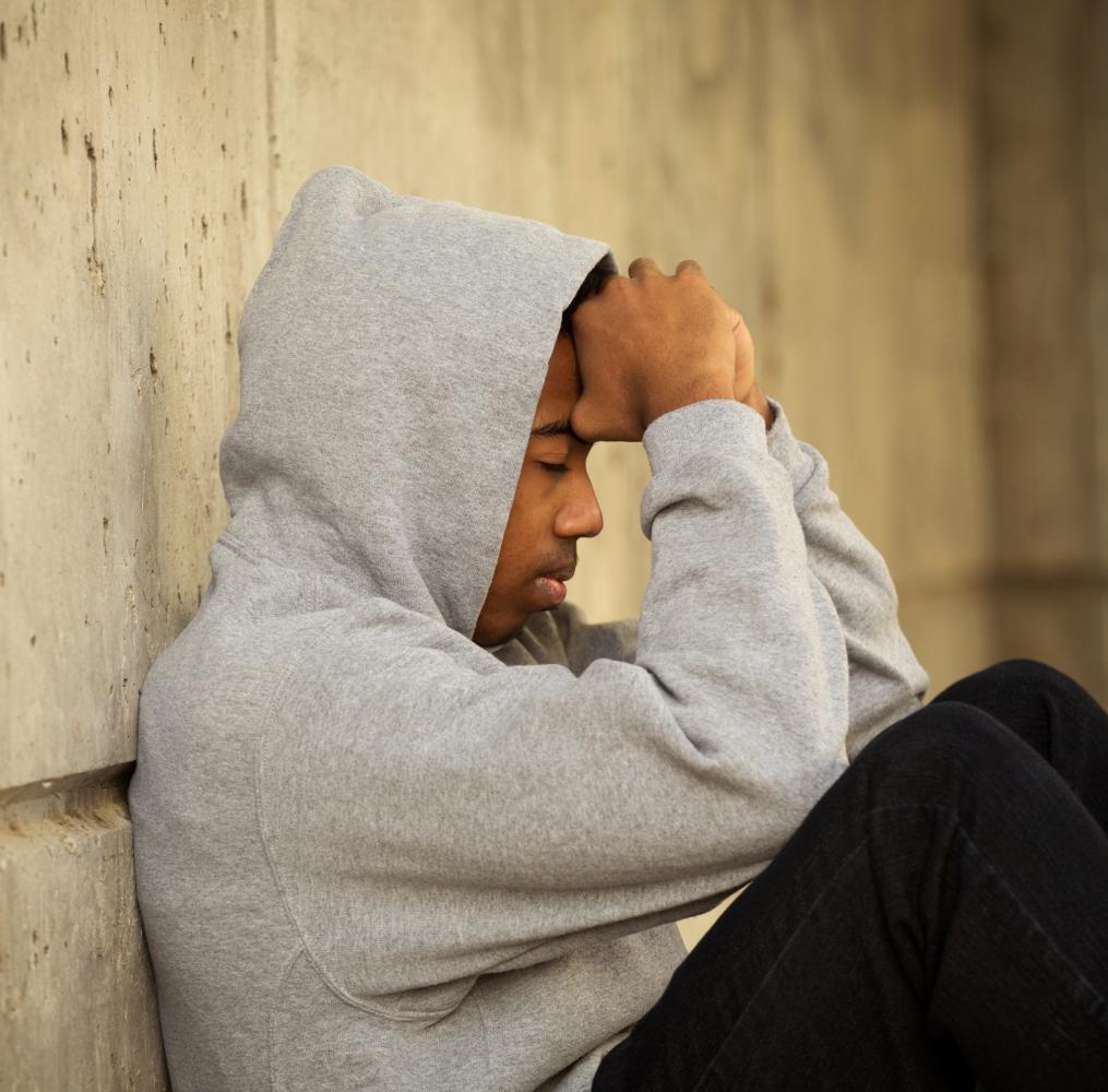 Teenage boy seated with arms covering his face.