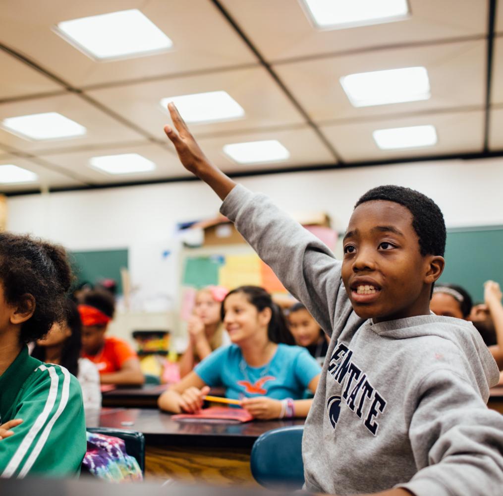 Elementary student enthusiastically raising hand in a classroom.