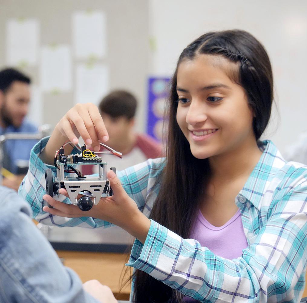 Adolescent student holding a robot in a classroom.