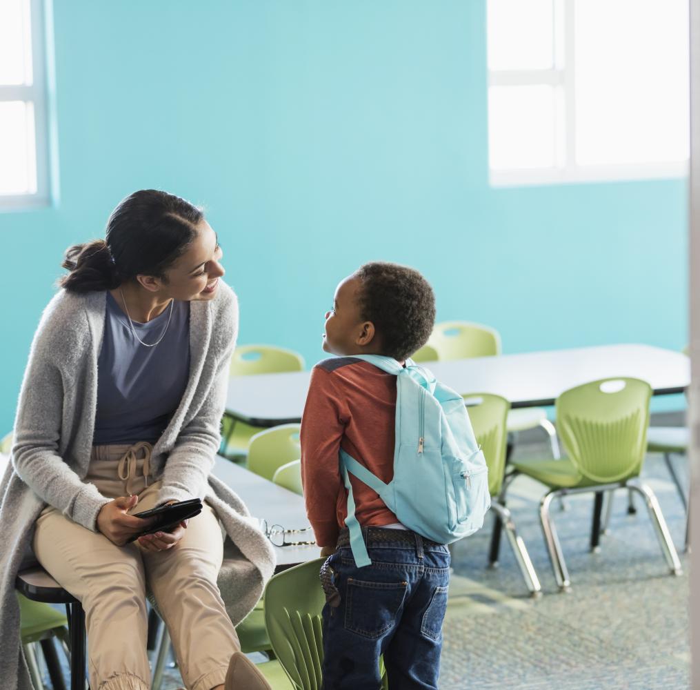 Teacher talking to an elementary student in an empty classroom.