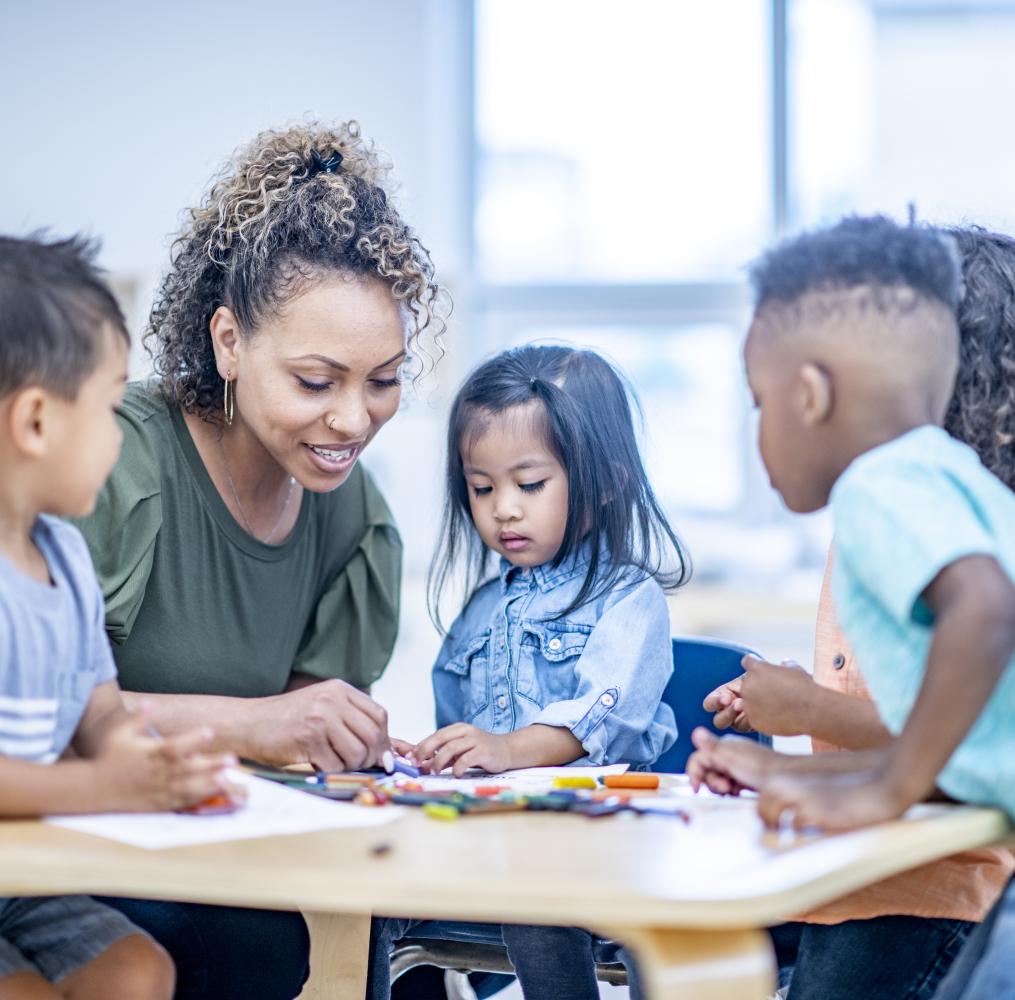 A teacher helping preschool students at a table in a classroom.