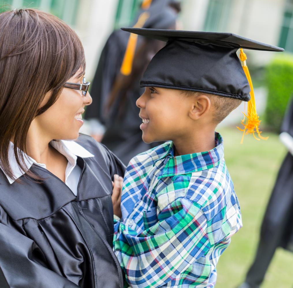 Woman in a graduation gown smiling with a child wearing a graduation cap.