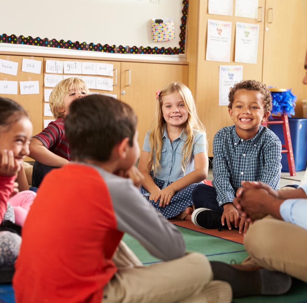 Teacher with elementary students seated on the floor.