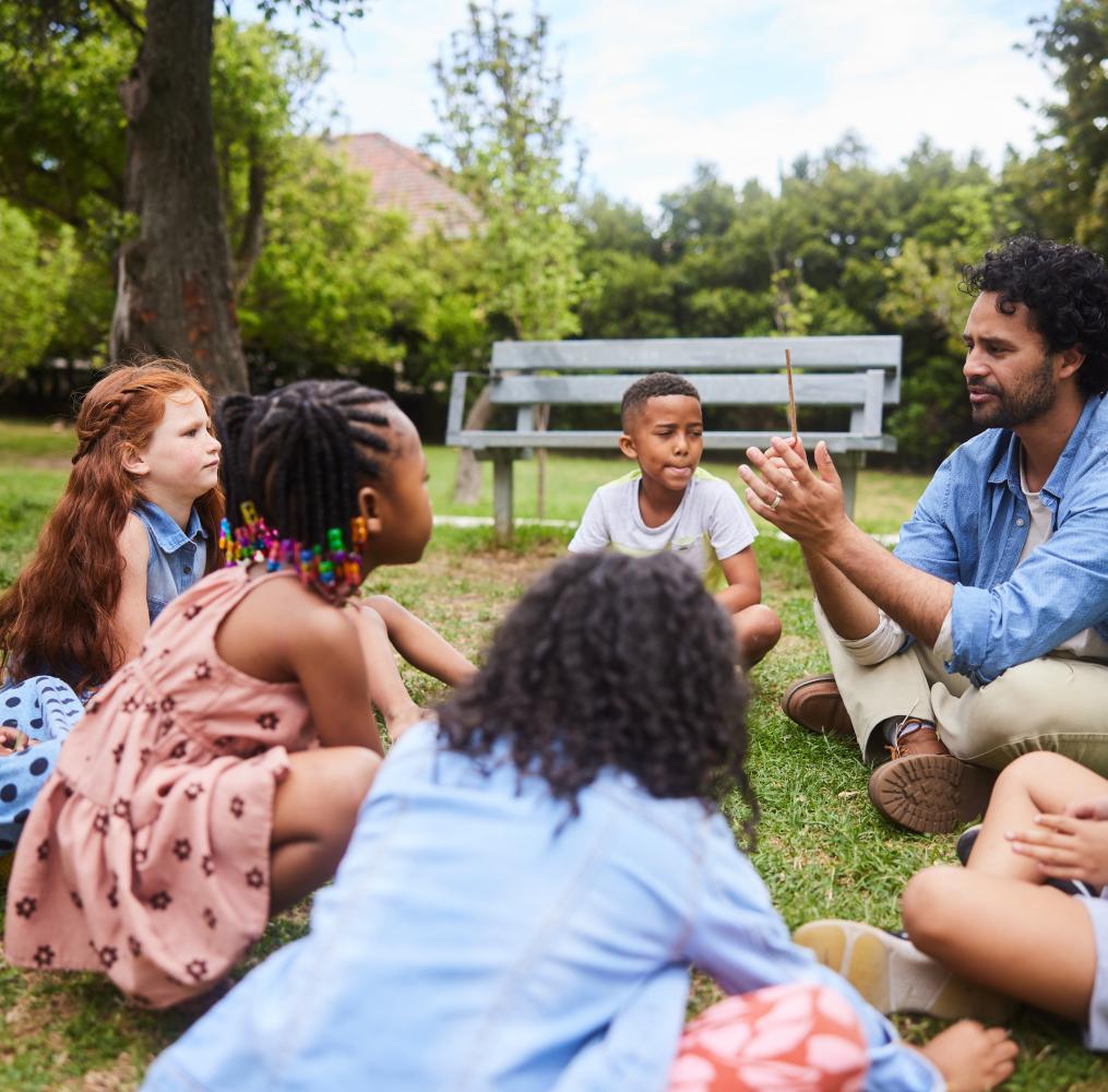 Teacher and students seated on the ground outside.