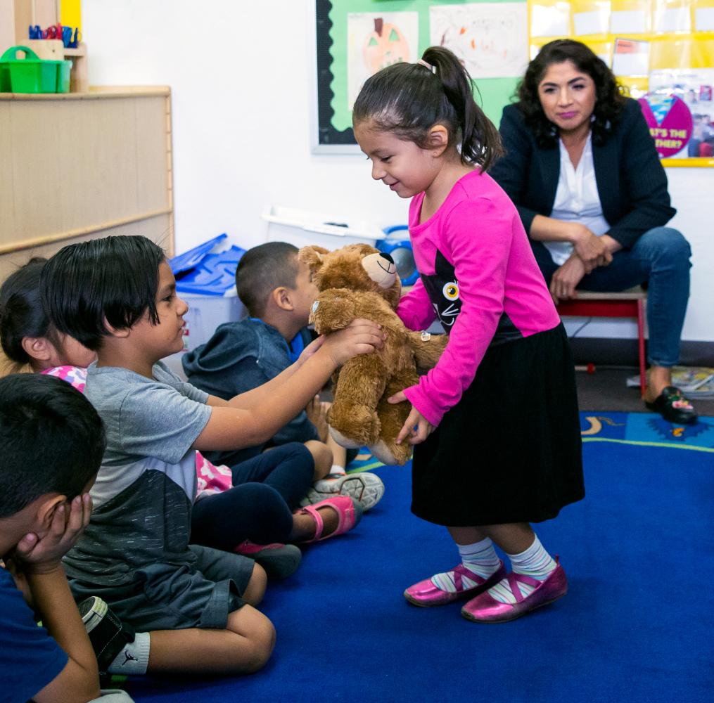 Teacher watching students interact with a teddy bear.