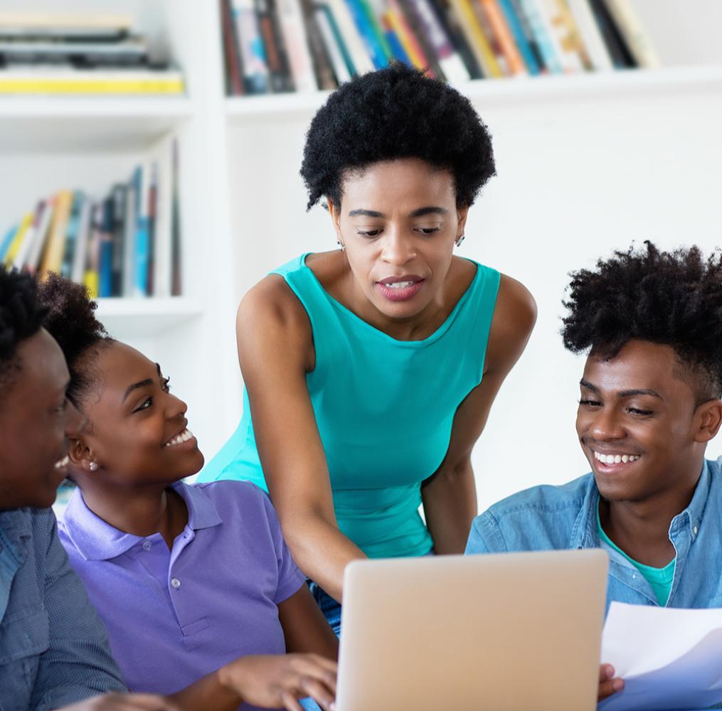 A teacher helping students with an assignment on a laptop.