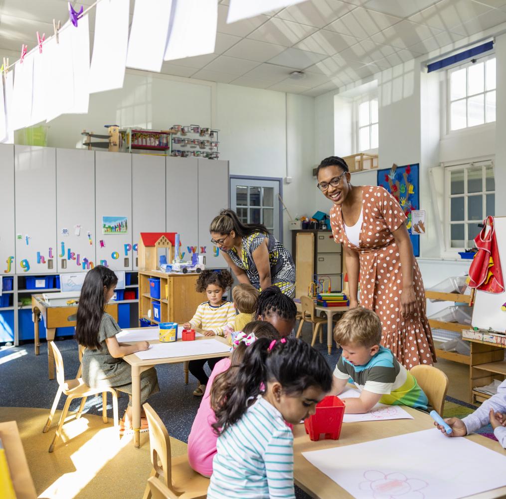 Two preschool teachers assisting students with an project.