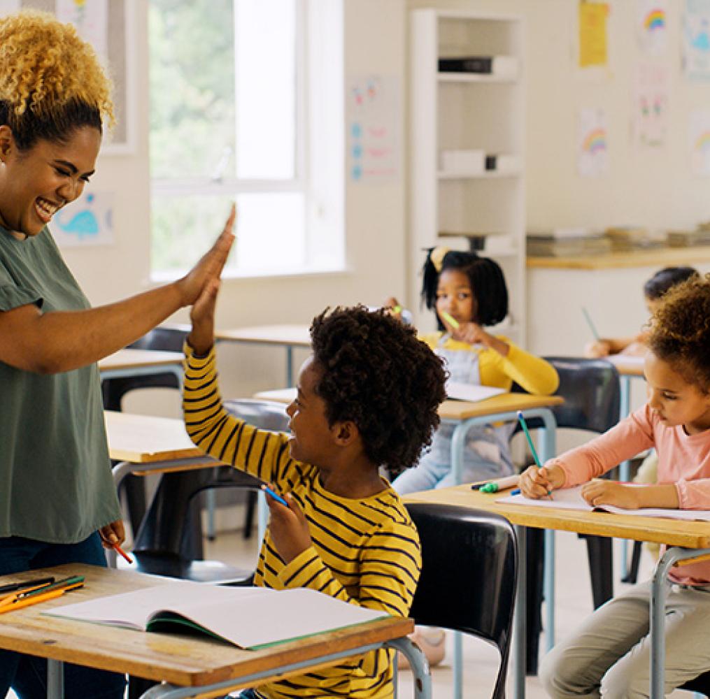 A teacher giving a student a high five in a classroom.