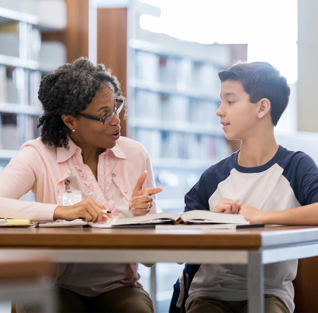 An educator helping a middle school student in a library.