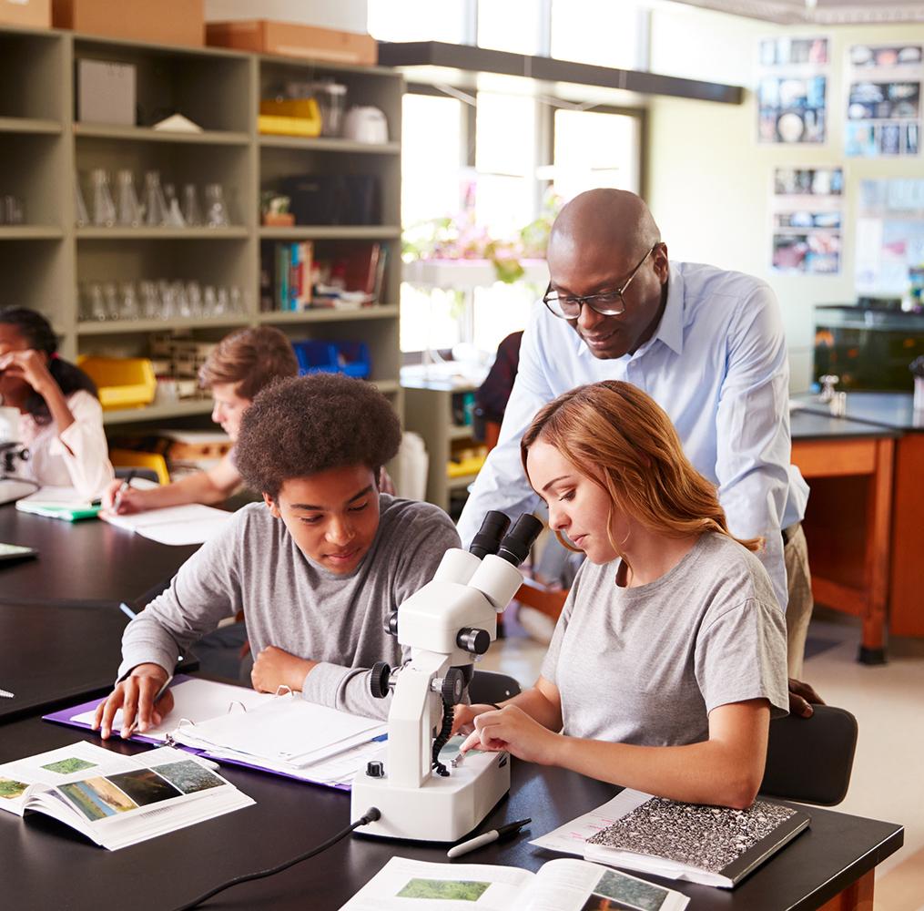 A teacher helping high school students use a microscope.