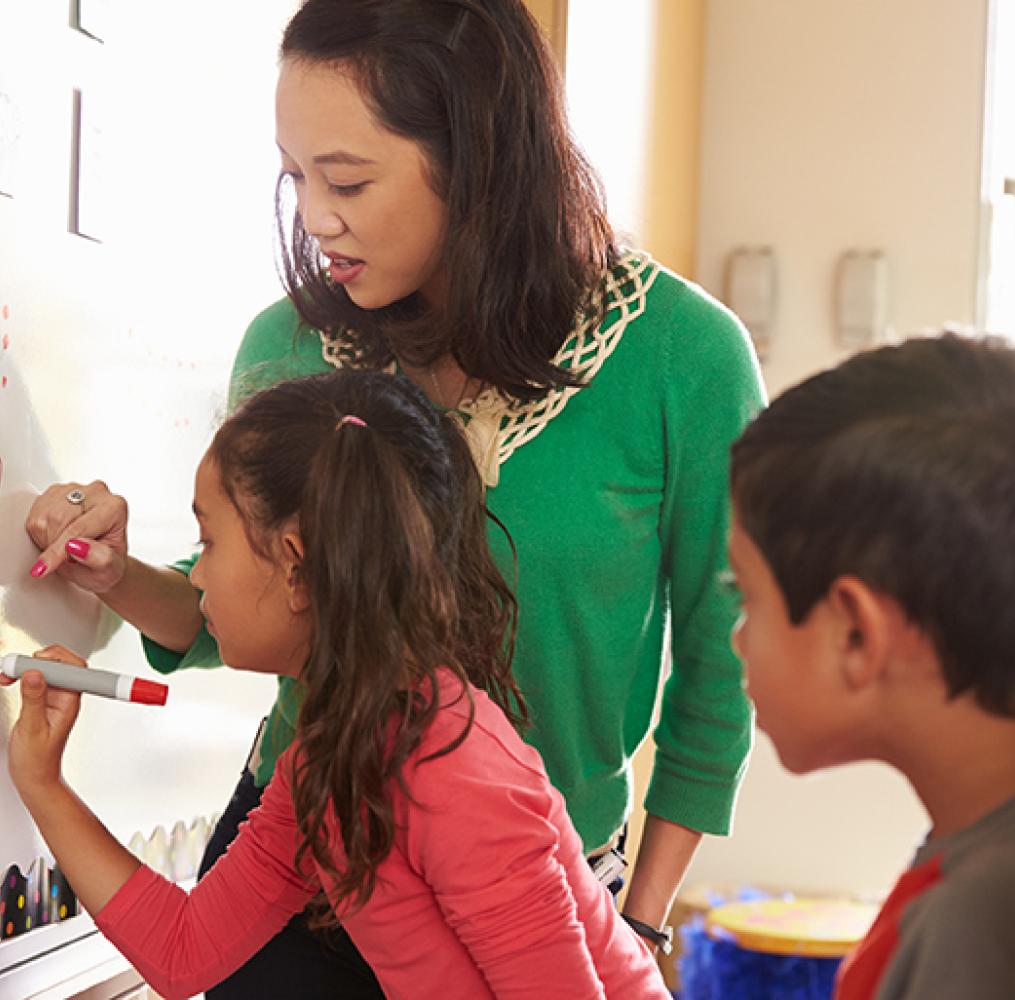 Teacher helping a student with an equation on a whiteboard.
