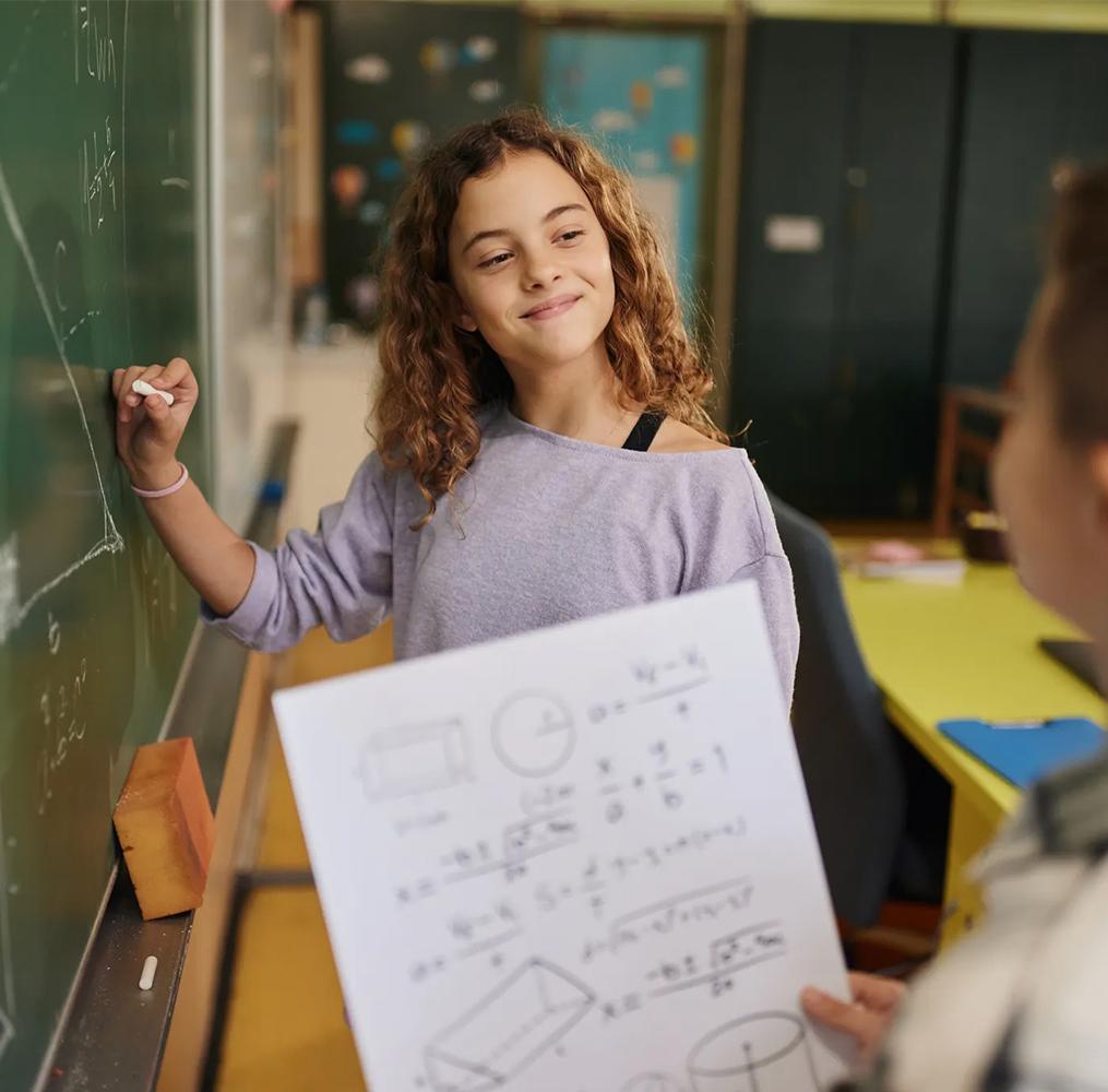 A middle school student working on a math equation on a blackboard.