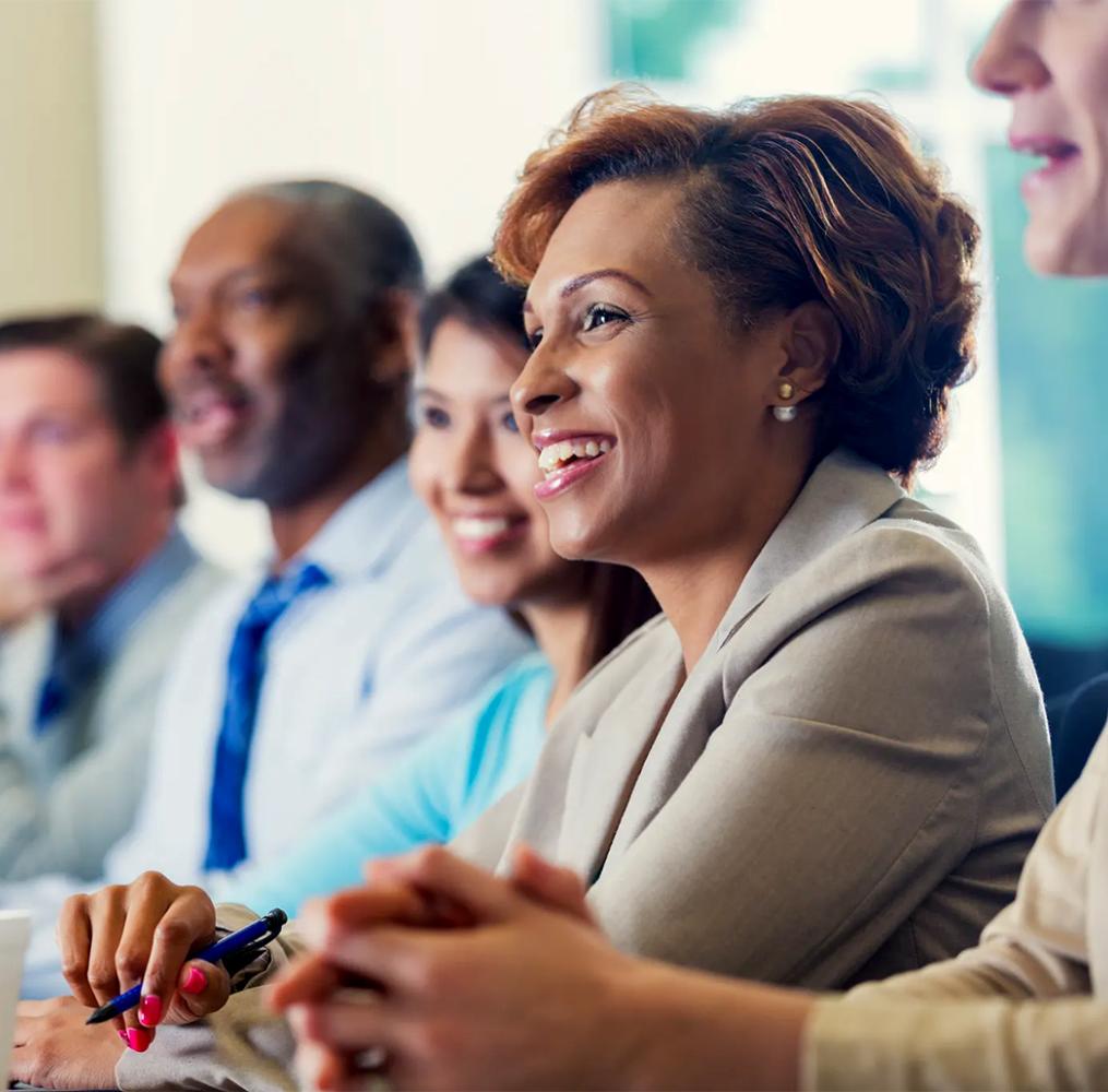 A smiling woman sitting at a conference table with others.