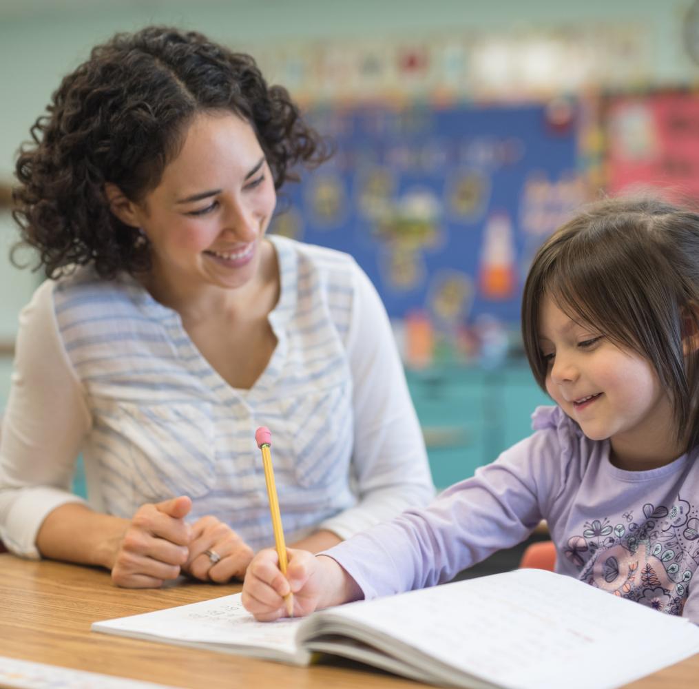 A teacher assists an elementary student with an assignment in a classroom.