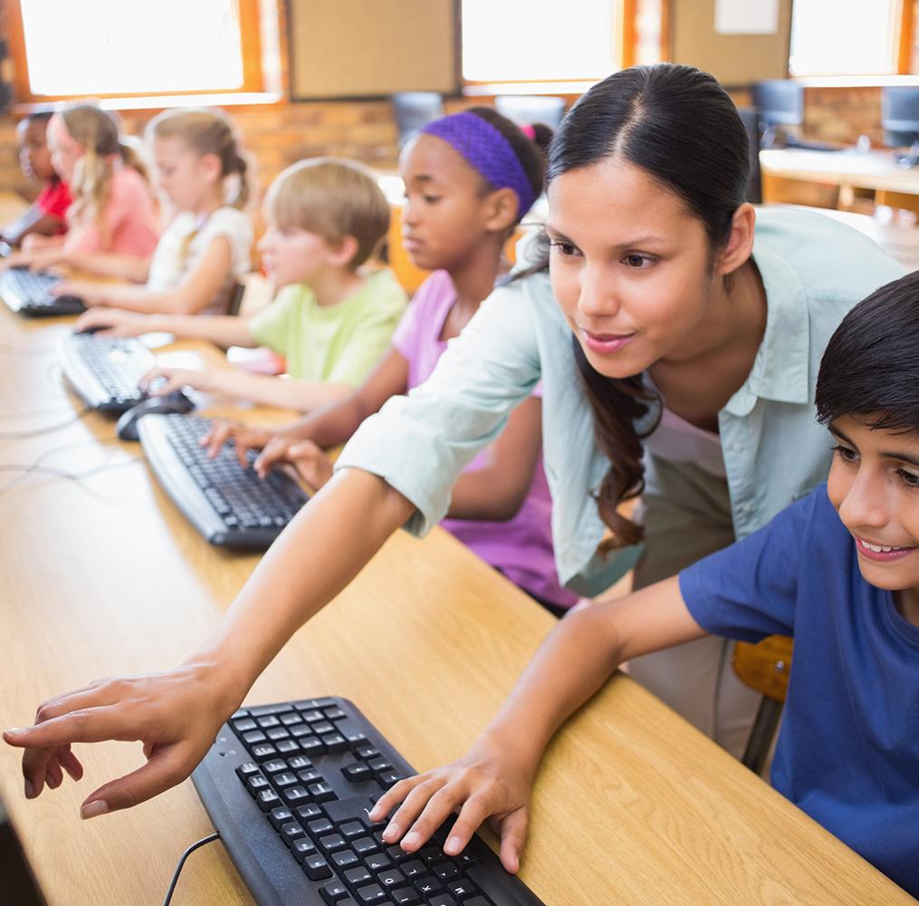 A teacher assists a middle school student in a computer class.