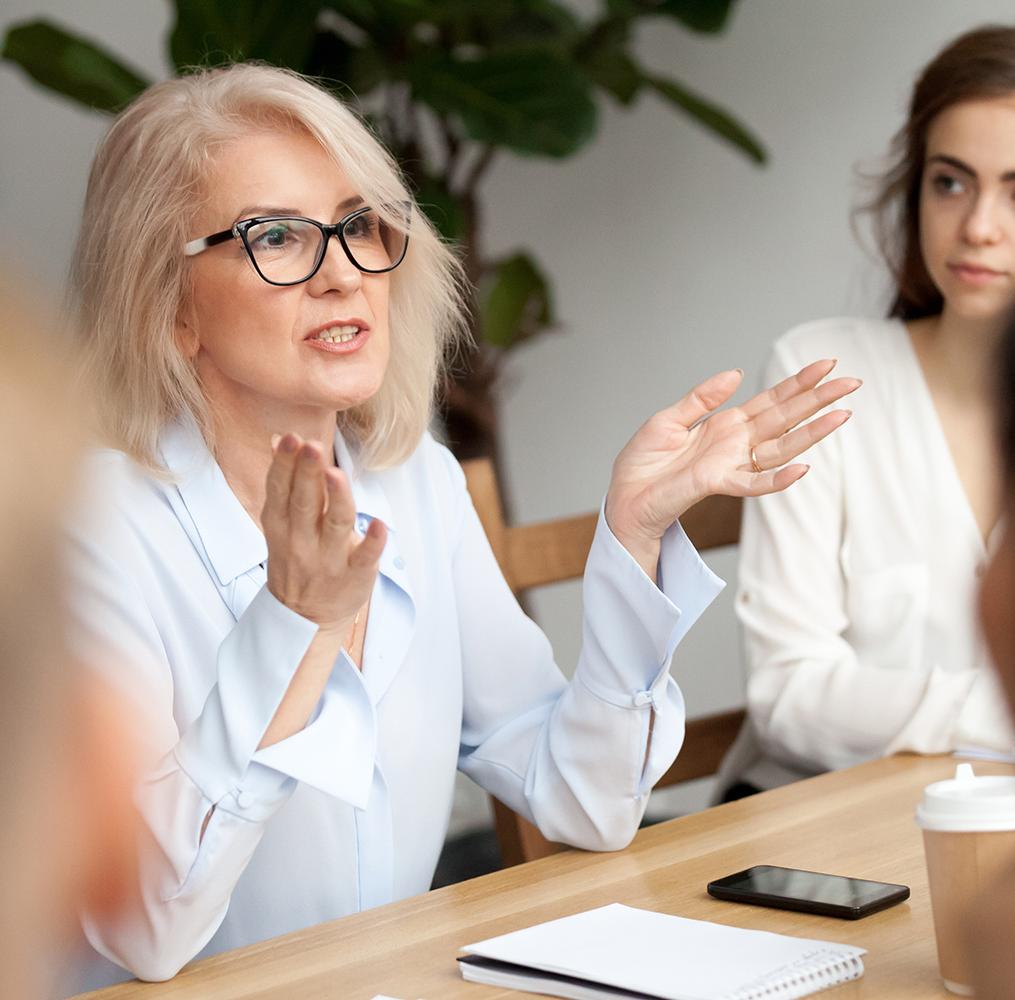 A woman seated at a table having a discussion with peers.