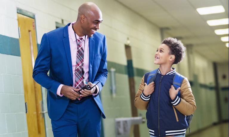 Elementary student walking with principal in school hallway