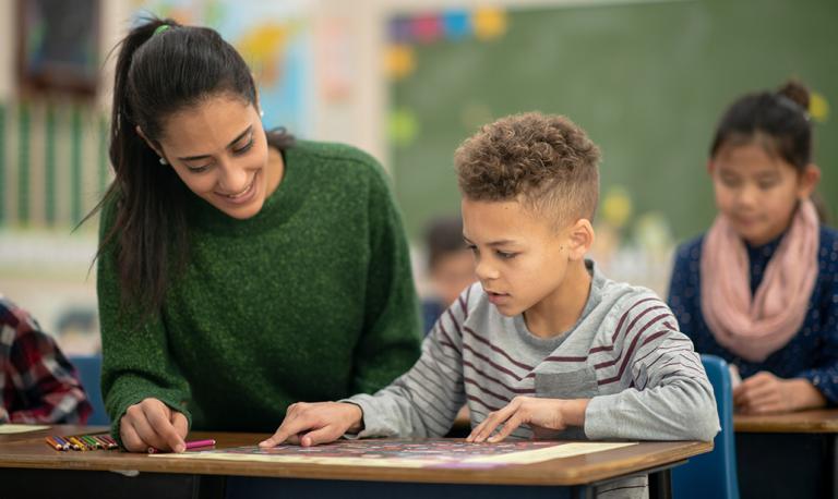 A young teacher helping an elementary student with an assignment.