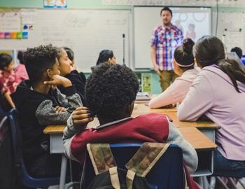 teacher in front of a whiteboard facing high school aged students