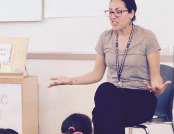 teacher seated in front of elementary aged students