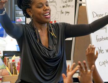 An elementary school teacher with arms raised in front of children