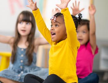 elementary aged students with both hands raised