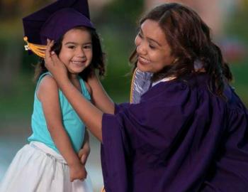 Woman in a graduation gown crouching next to a girl with a graduation cap