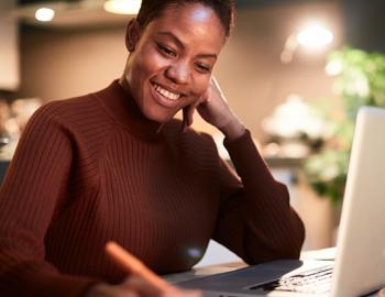 Woman seated in front of a laptop smiling and taking notes