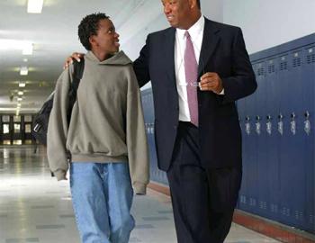 Male educator and male high school-aged student walking in a school hallway