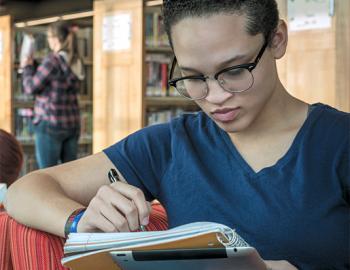 College aged woman writing in a notebook in a library