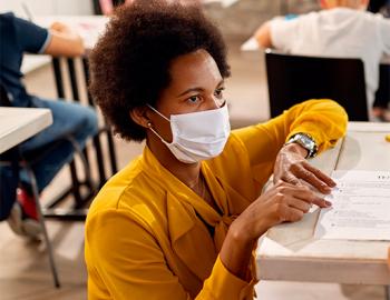 African American teacher wearing a mask kneeling next to a student