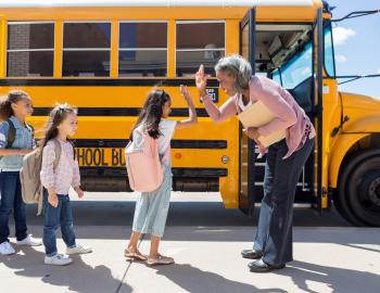 Principal giving an elementary student a high five in from of a school bus.