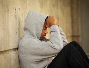 Teenage boy seated with arms covering his face.