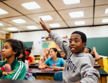 Elementary student enthusiastically raising hand in a classroom.