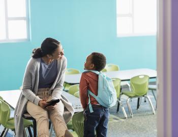 Teacher talking to an elementary student in an empty classroom.