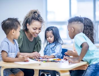 A teacher helping preschool students at a table in a classroom.