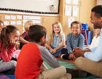 Teacher with elementary students seated on the floor.