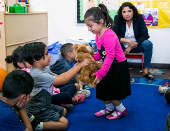 Teacher watching students interact with a teddy bear.