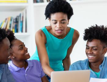 A teacher helping students with an assignment on a laptop.