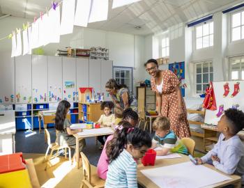 Two preschool teachers assisting students with an project.